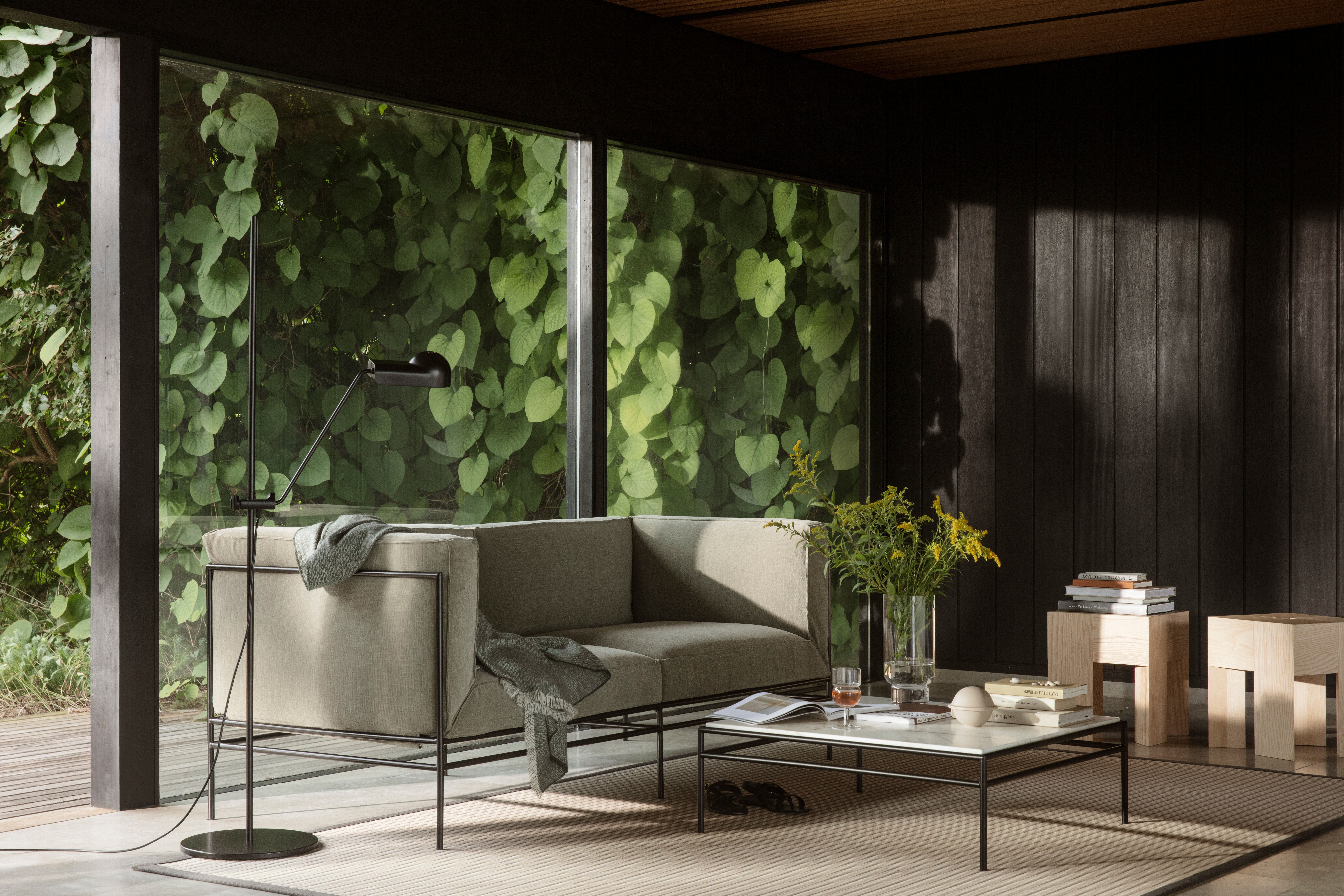 Zweisitziges Sofa mit schwarzem Gestell vor großer Fensterfläche mit Blick ins Grüne