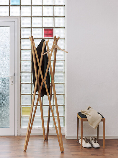Garderobe aus Holz mit Jacke und Hocker vor Wand aus Glasbausteinen