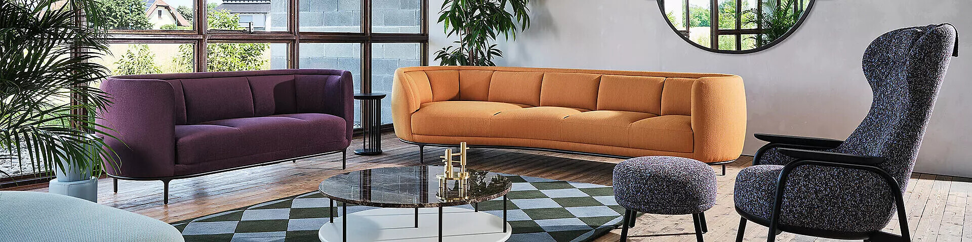 Wohnensemble von Wittmann mit runden Sofas und bezogenem Hochlehnsessel Zwei geschwungene Sofas in Orange und Violett, kombiniert mit Sessel und Couchtisch im WohnraumZwei geschwungene Sofas in Orange und Violett, kombiniert mit Sessel und Couchtisch im Wohnraum