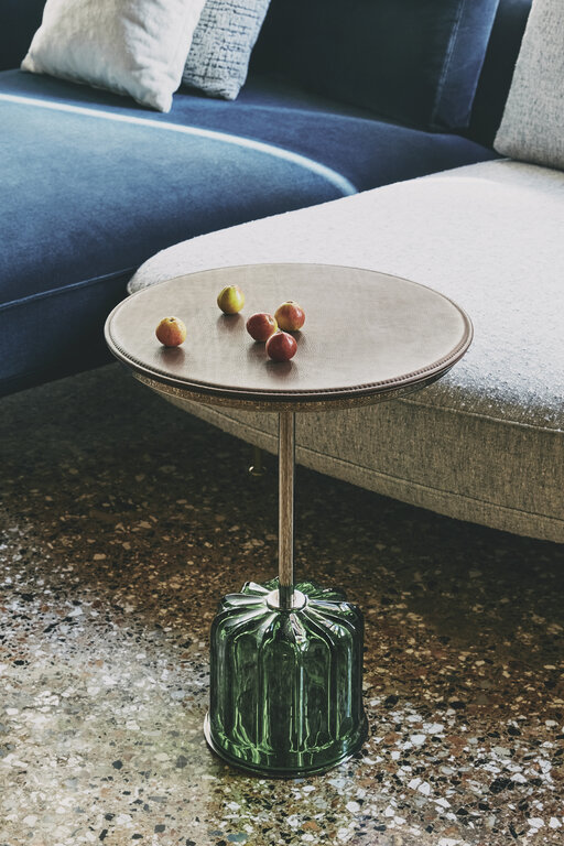 Acacia Grande Chestnut Murano verde von Wittmann Runder Beistelltisch mit strukturierter Glasbasis vor einem Sofa mit gemustertem Boden