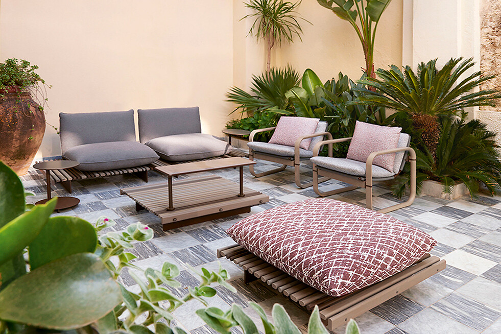 Loungekollektion von Giorgetti mit wetterfesten Sesseln und Kissen im begrünten Patio Outdoor-Möbel mit Loungesesseln, Bank und Bodenkissen auf gefliestem Patio