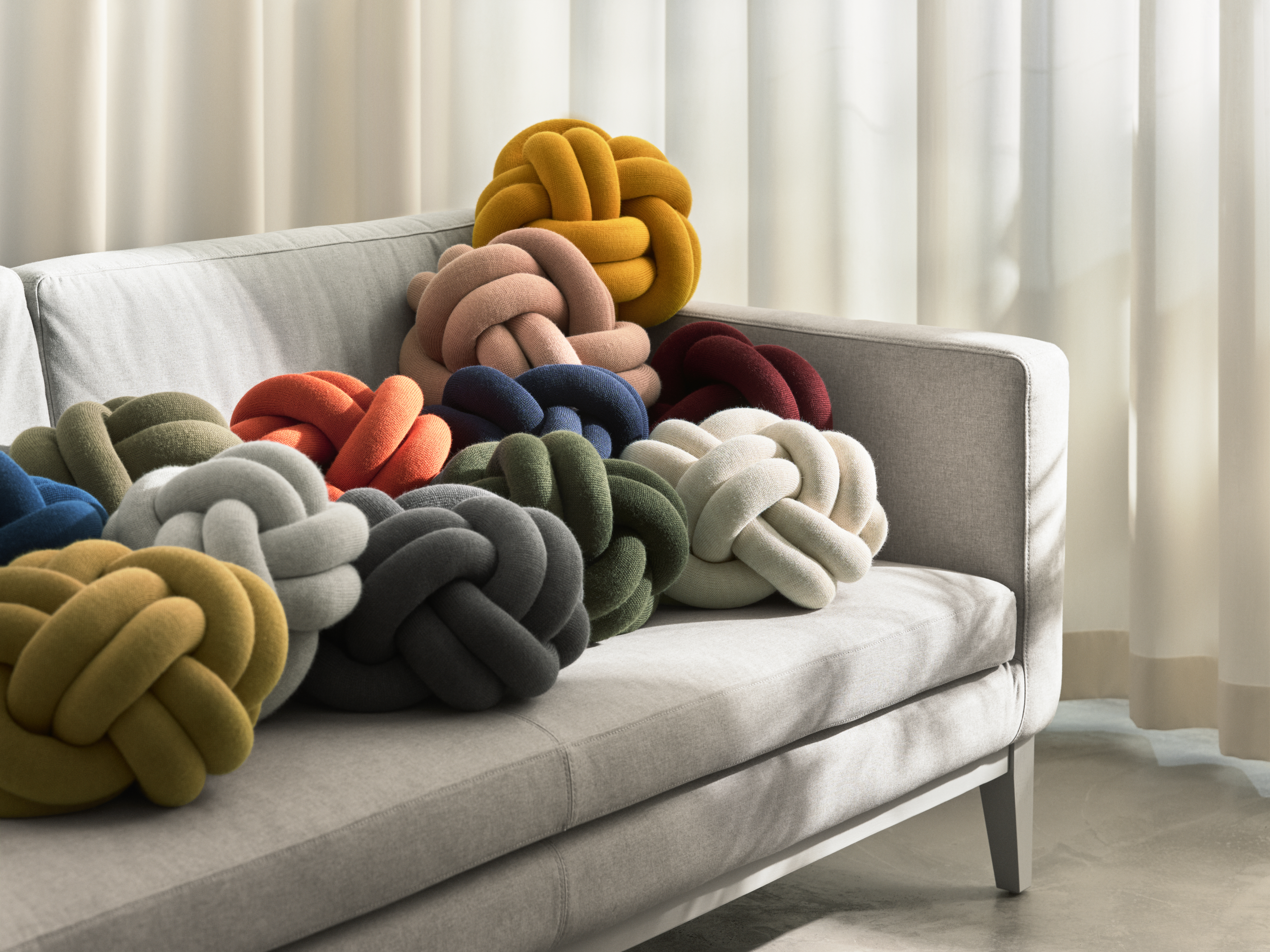 Knot Kissen von Design House Stockholm in vielfältiger Farbgebung Mehrere Knot-Kissen von Design House Stockholm in verschiedenen Farben auf einem Sofa arrangiert