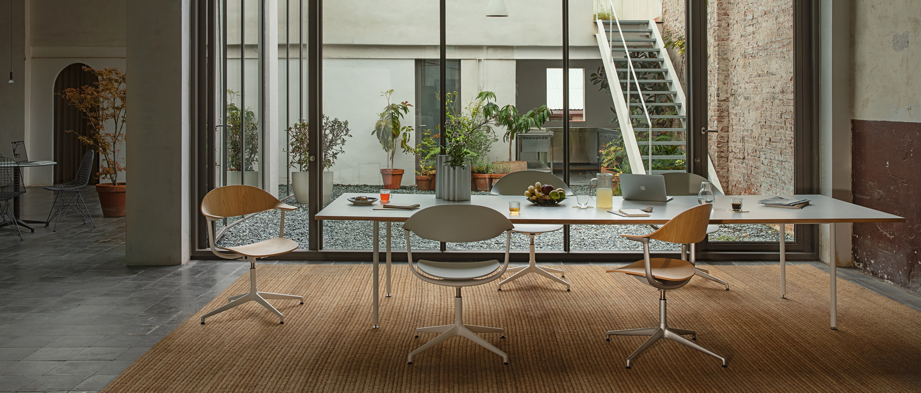 Der Essbereich ist mit mehreren Mynt Stühlen von Vitra ausgestattet, die um einen langen Tisch arrangiert sind. Durch große Fenster blickt man auf eine begrünte Terrasse, was dem Raum eine helle und offene Atmosphäre verleiht.