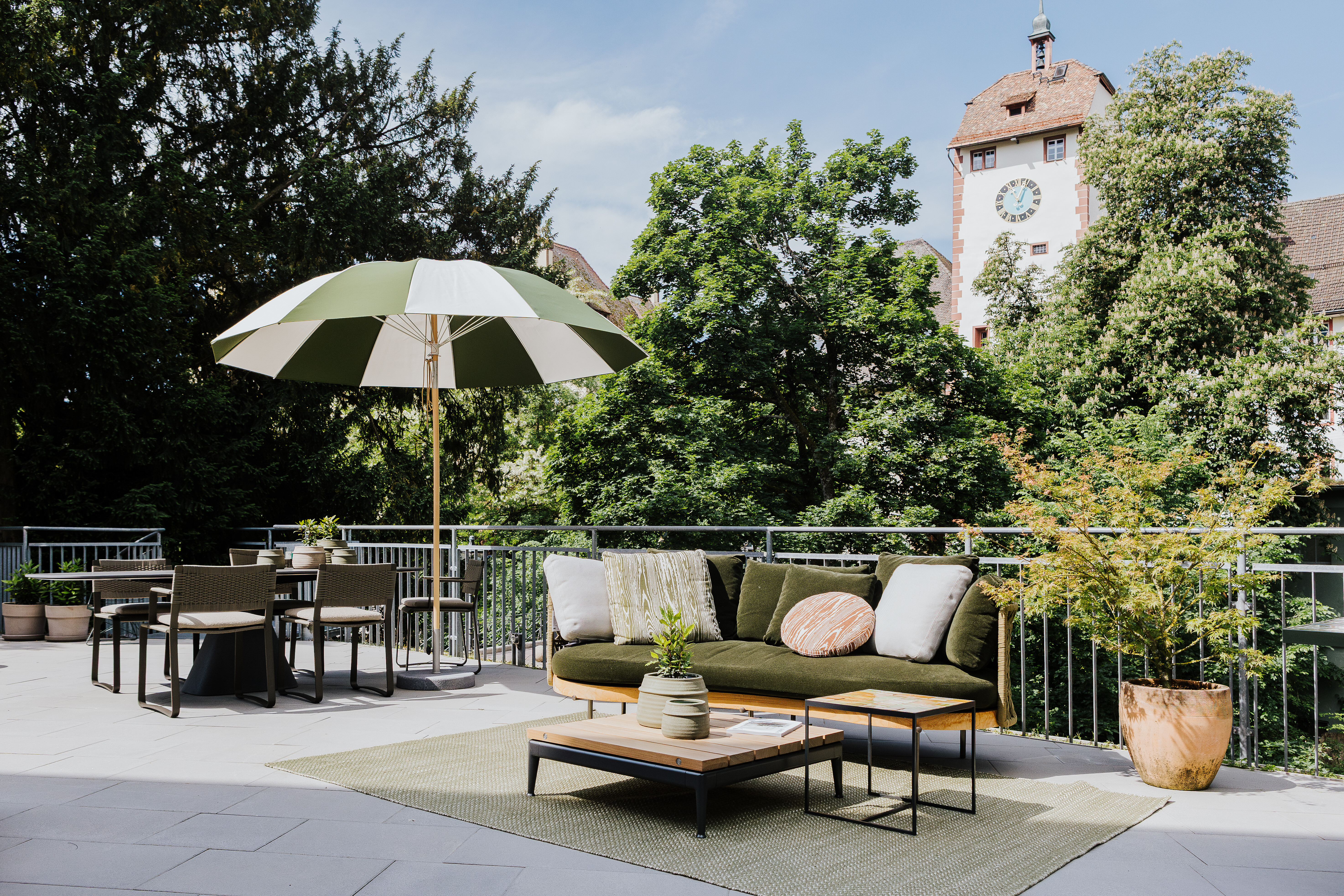 Gartenmöbel auf Terrasse in Waldshut mit grün-weißem Schirm, Loungemodulen und Esstischgruppe.  