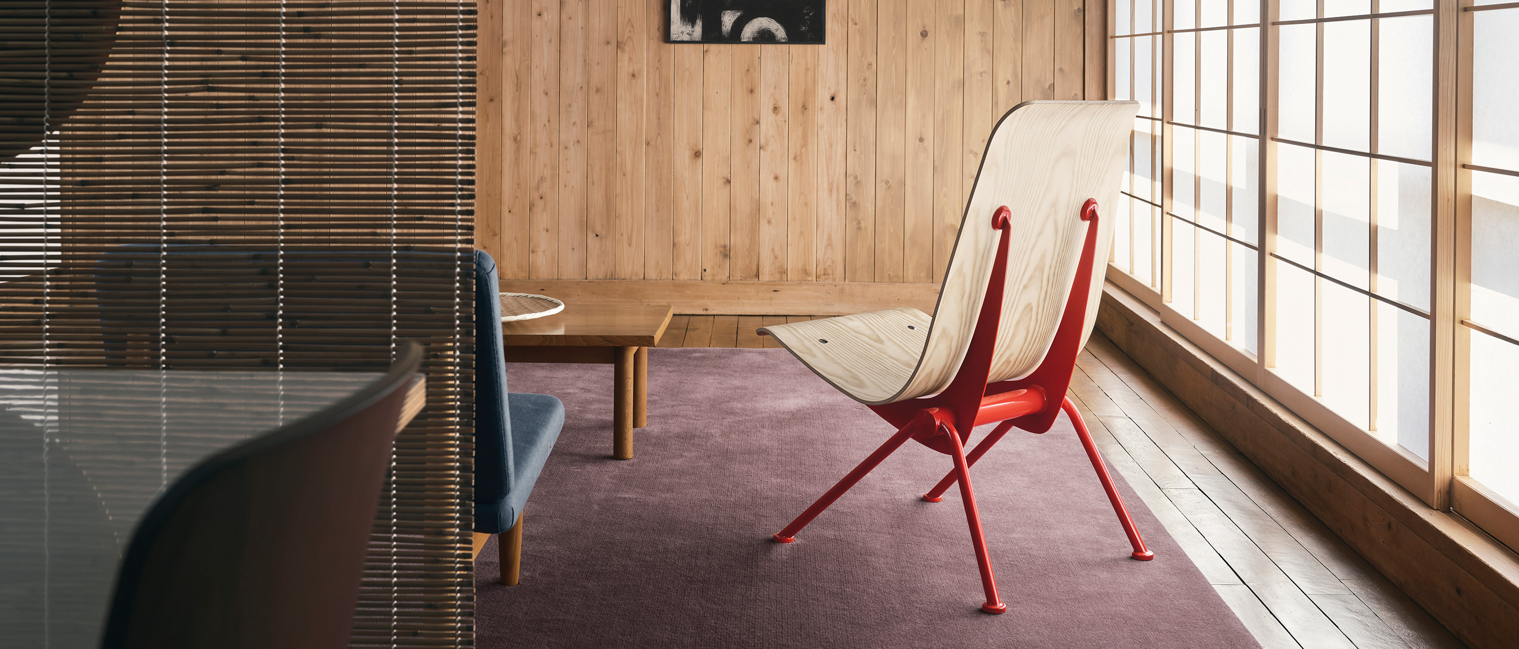 Antony Sessel von Vitra (limitierte Edition) in Holzinterieur. Ein roter Antony Sessel von Vitra, Teil einer limitierten Edition, steht prominent in einem Raum mit Holzwänden und einem großen Fenster. Sein einzigartiges Design fügt sich harmonisch in das warme Ambiente ein.