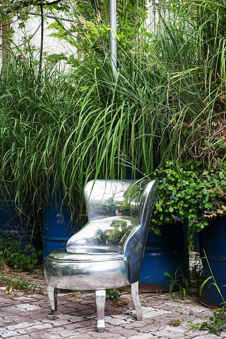 Skulpturaler Sessel aus hochglänzendem Aluminium vor dichtem Grün