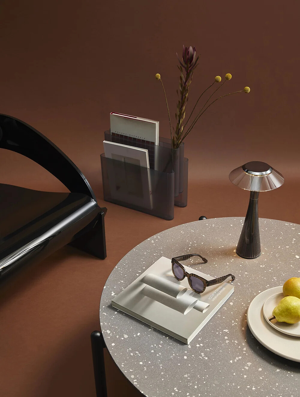 Designobjekte von Kartell – stilvolle Inszenierung mit Tisch und Accessoires Runder Tisch mit Sonnenbrille, Vase, Lampe und Zeitschriftenständer auf Braunton